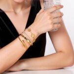 Close-up of four GIVCHO 18K gold plated bangle bracelets with colorless cubic zirconia stones, stacked on a wrist.