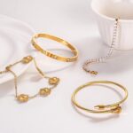 Close-up of four GIVCHO 18K gold plated bangle bracelets with colorless cubic zirconia stones, stacked on a wrist.