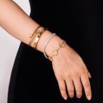 Close-up of four GIVCHO 18K gold plated bangle bracelets with colorless cubic zirconia stones, stacked on a wrist.