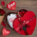 Red heart-shaped gift box open to reveal a 12 oz insulated tumbler, bath bomb, mirror, soap roses, and other spa items.