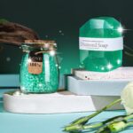 An emerald green spa gift basket featuring a bath bomb, body salt, candle, gem soap, and a stainless steel wine mug.